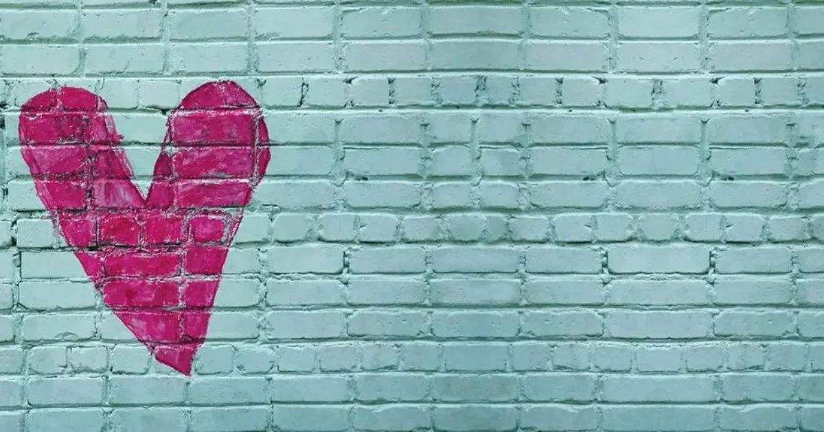 A hand-painted bright pink heart on a light blue brick wall.