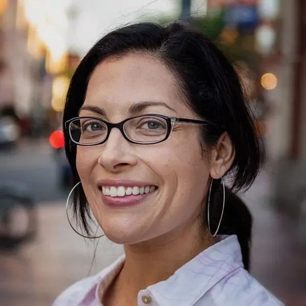 A woman with dark hair and glasses smiling at the camera.