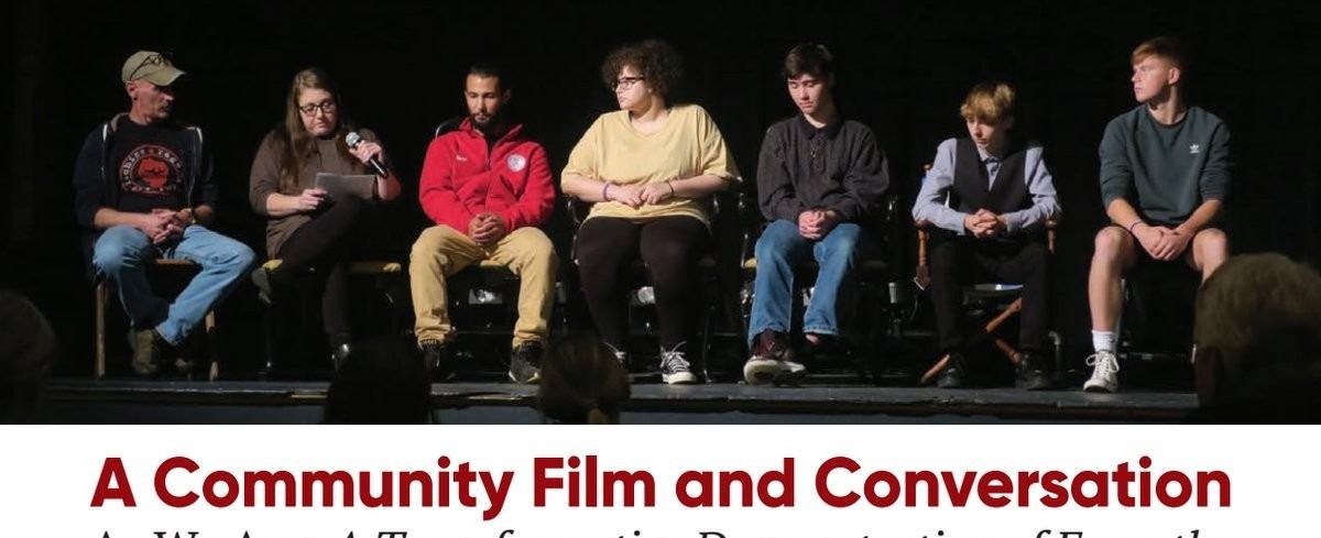 A panel of seven people sitting in a row on a stage during a community film event.