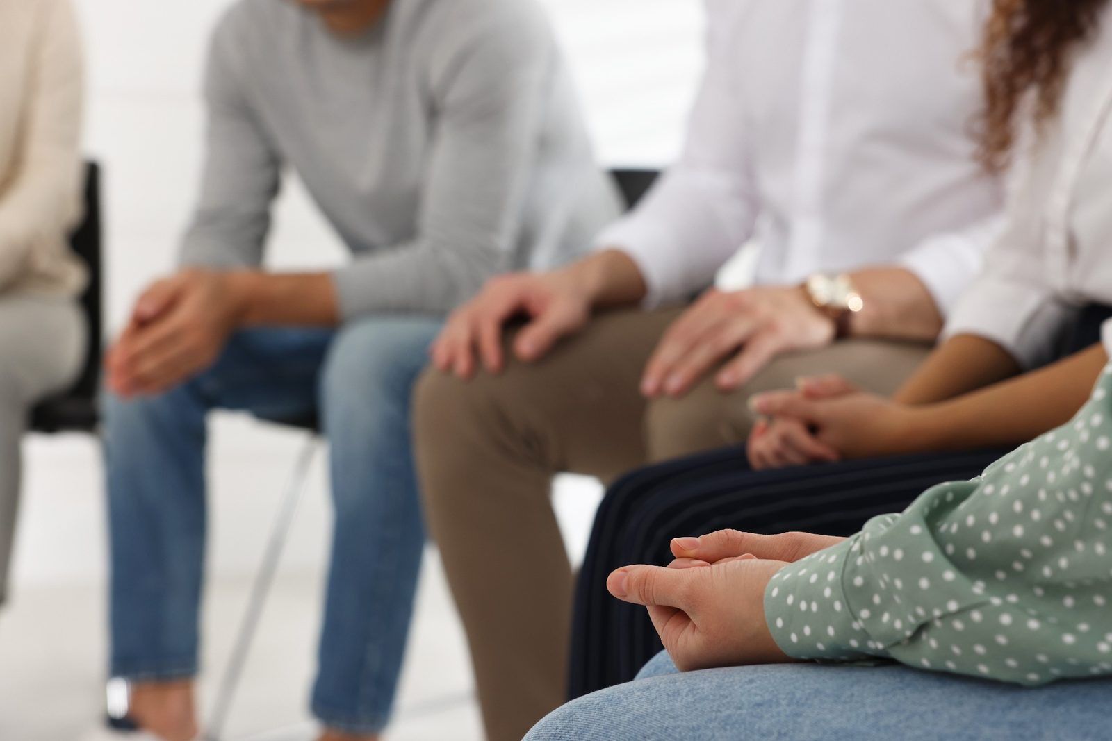 A group of people sitting in a circle during a meeting, with focus on their hands resting in their laps.