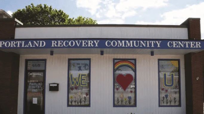 The Portland Recovery Community Center building with windows decorated with a rainbow, a heart, and the letters WE and U.