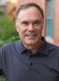 A middle-aged man with short, graying hair wearing a dark polo shirt.