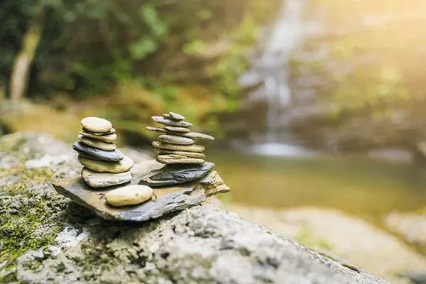 Two stacks of balanced stones resting on a mossy rock in front of a waterfall.