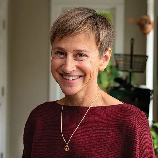 A woman with short brown hair smiles while wearing a maroon sweater and a gold pendant necklace.