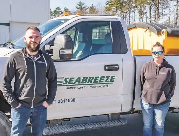 A man and a woman standing in front of a white Seabreeze Property Services pickup truck.