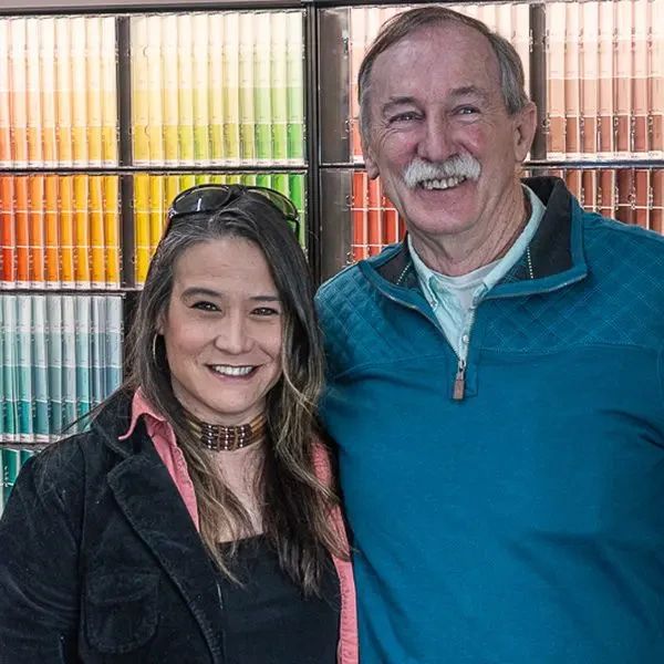 A smiling woman and man standing in front of a wall of paint color samples.
