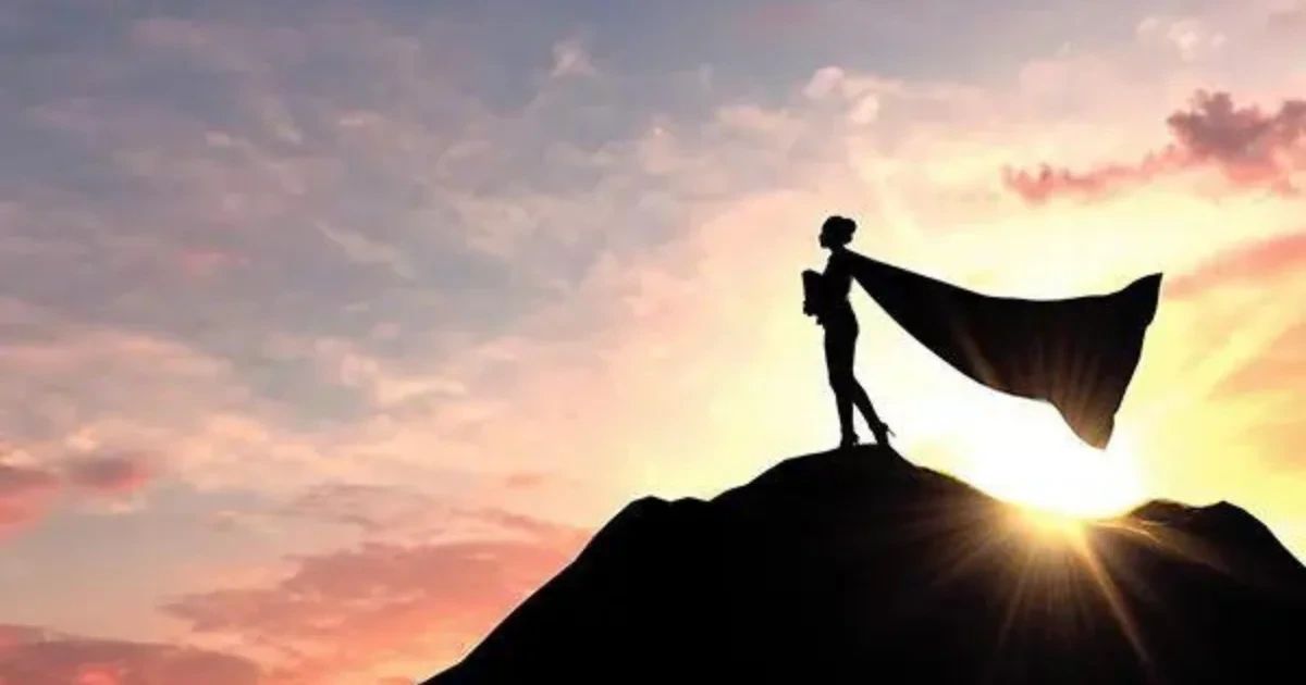 Silhouette of a person wearing a cape standing atop a hill against a sunset sky.