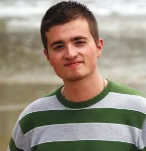 A young man wearing a green and gray striped sweater looking at the camera.