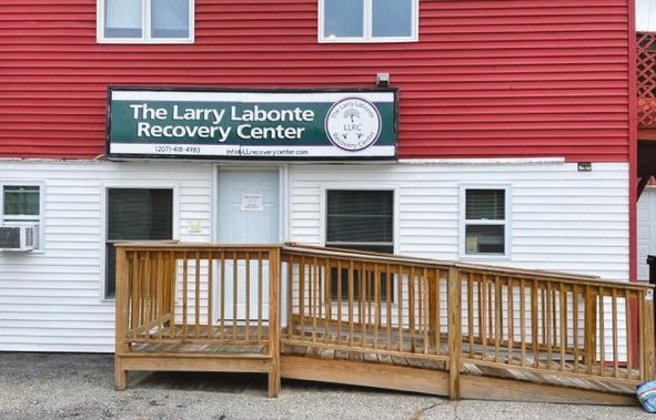 A red and white building with a wooden wheelchair ramp leads to the door, where a sign above warmly welcomes visitors to the Larry Labonte Recovery Center.
