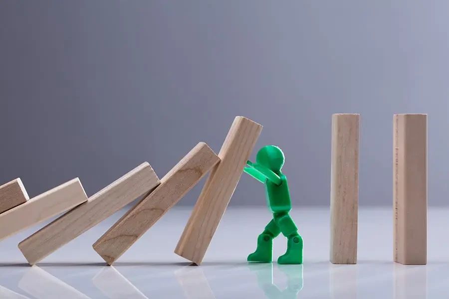 A green toy figure stops a falling wooden block from toppling the rest of the row.