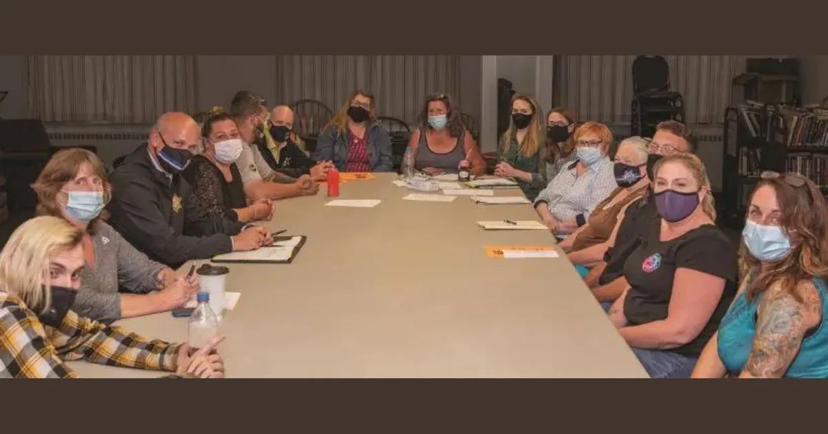 A group of people wearing face masks sit around a large conference table.
