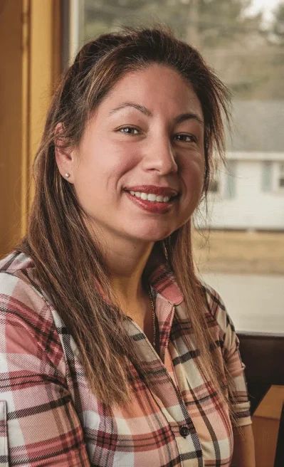 A smiling woman wearing a plaid shirt looks toward the camera.