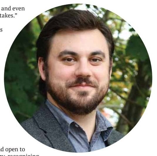 A headshot of a smiling man with a beard, wearing a collared shirt and blazer.