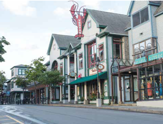 A street view of storefronts in a coastal town, featuring a prominent red lobster sign above a restaurant.