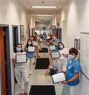 A group of medical professionals in scrubs and face masks standing in a hallway, each holding a certificate.