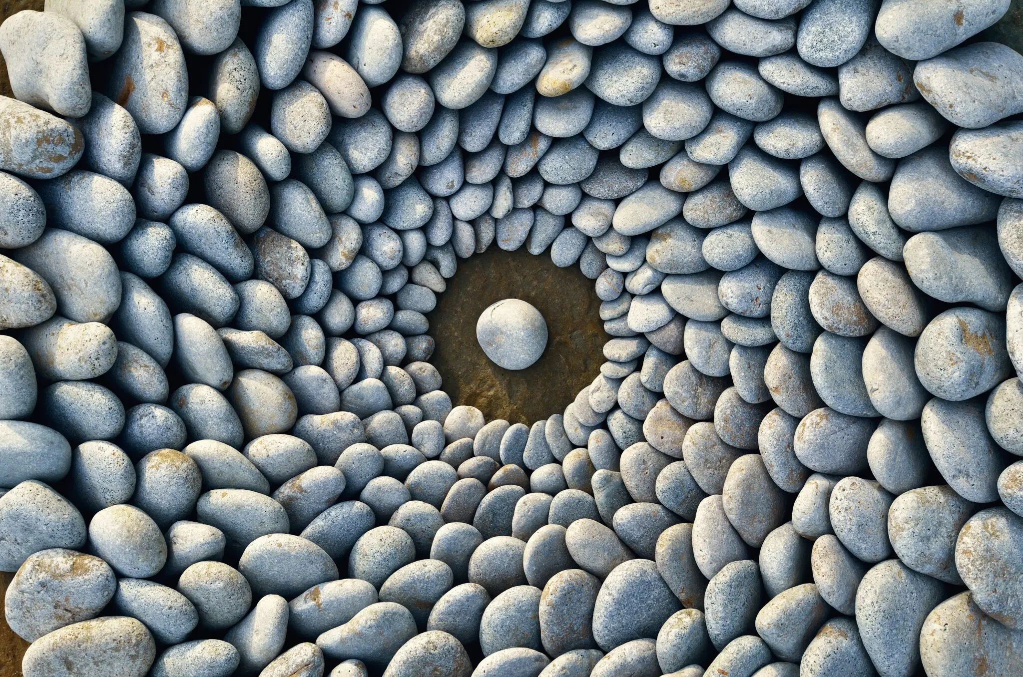 Smooth river stones arranged in concentric circles with one centered stone in a dark pool.