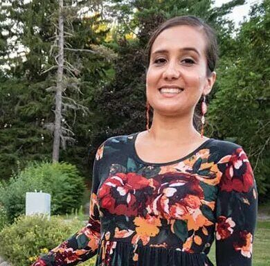 A smiling woman wearing a long-sleeved dress with a dark floral print and long dangling earrings.
