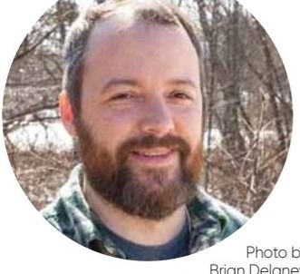 Headshot of a smiling man with a beard, cropped into a circle against a background of trees.