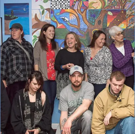A diverse group of adults posing in front of a colorful wall mural made of painted tiles.