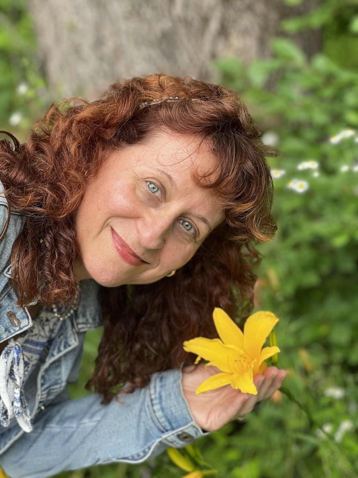 Carole Fontaine smiling outdoors among green leaves, holding a yellow lily.