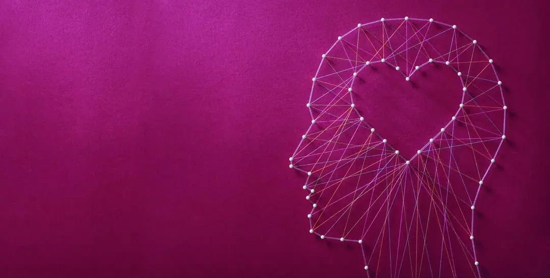 String art of a human profile outline containing a heart shape, created with pins and multicolored thread on a purple background.