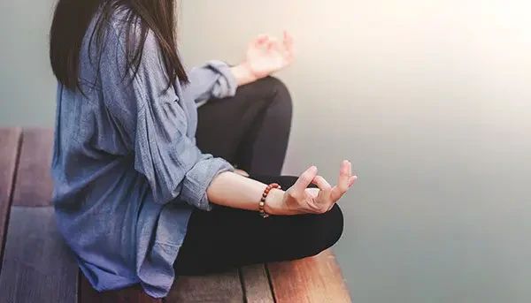 A person sitting in a lotus position on a wooden deck with their hands resting on their knees.