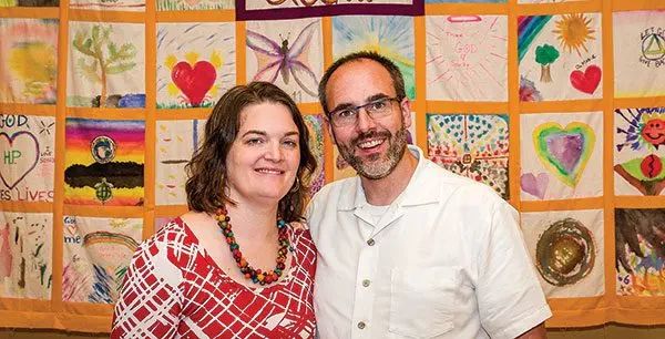A woman and a man standing in front of a wall covered in handmade art squares.