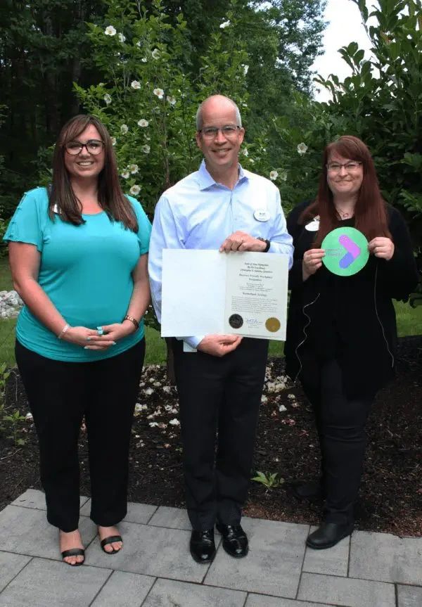 Three people stand outside holding a certificate and a green award badge.