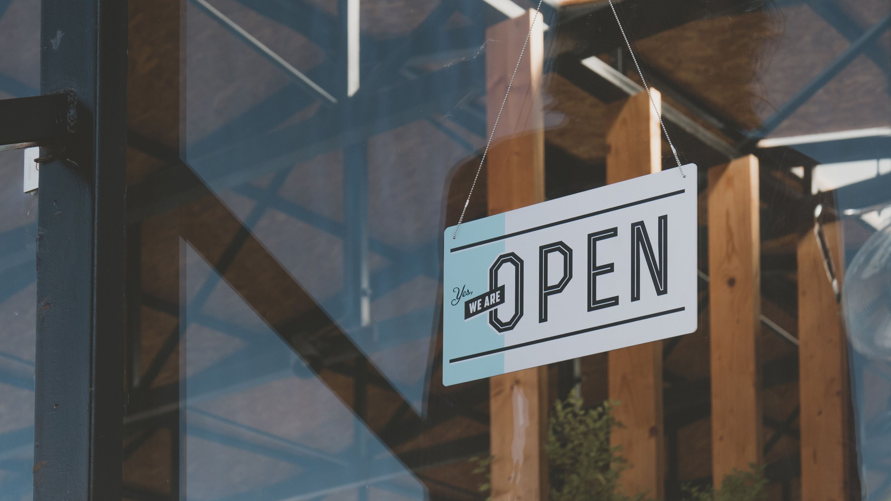 A sign hanging in a glass door that reads Yes, we are open.