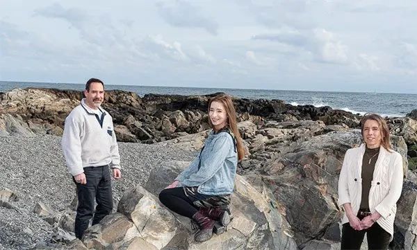 Three people posing on a rocky coastline by the ocean.