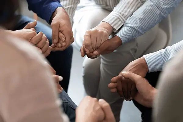A diverse group of people sitting in a circle, holding hands.