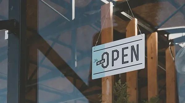 A rectangular sign hanging in a glass window that reads Yes, we are open.