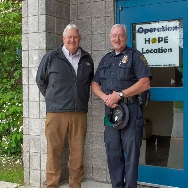 A man in a jacket and a police officer standing in front of a building entrance with an Operation HOPE Location sign on the glass door.