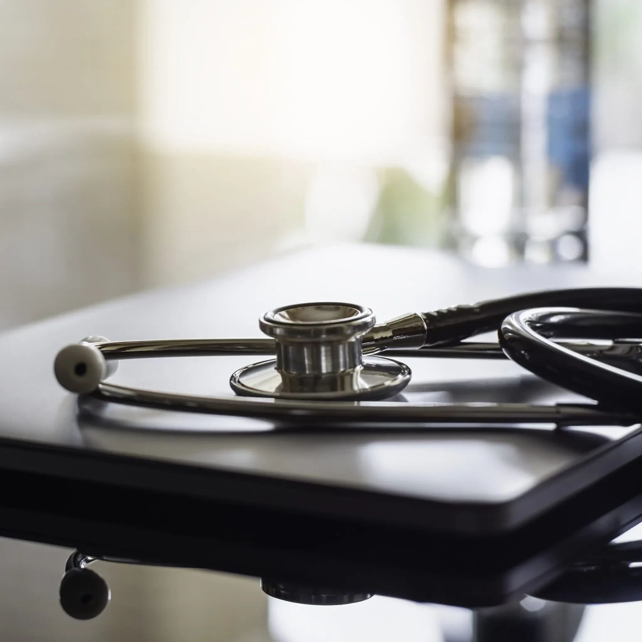 A stethoscope resting on a closed laptop on a dark desk.