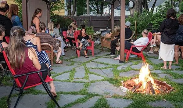 A group of people sitting on chairs around a fire pit in a stone patio area.