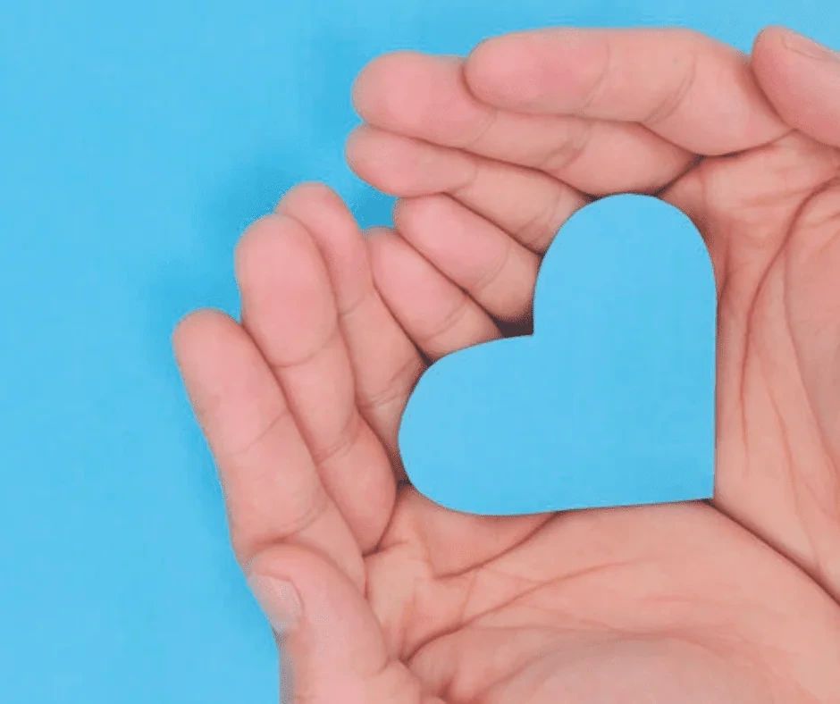 Cupped hands holding a blue paper heart.