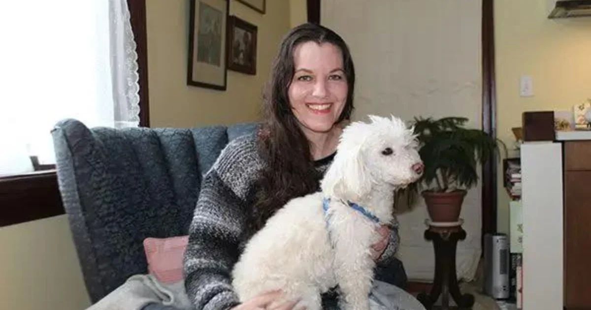 A woman with long dark hair smiling while holding a small white dog in her lap.