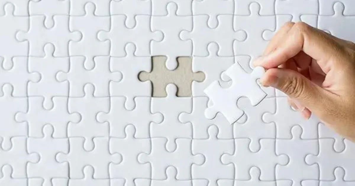 A hand holding the final white puzzle piece above an empty slot in a completed puzzle.