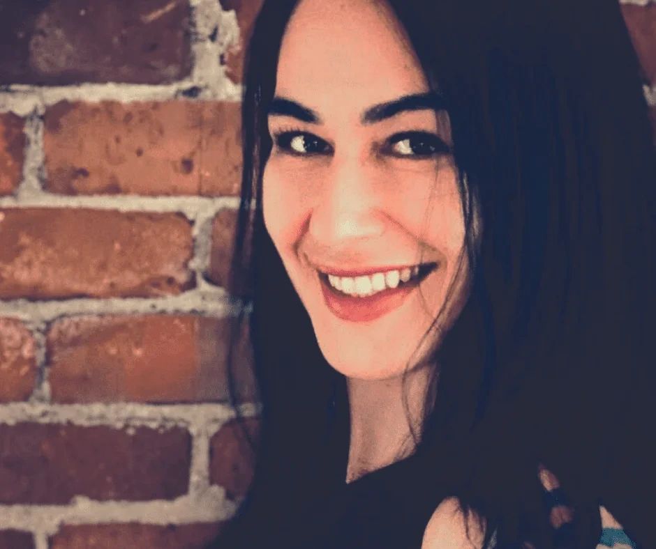 A smiling woman with dark hair in front of a brick wall.