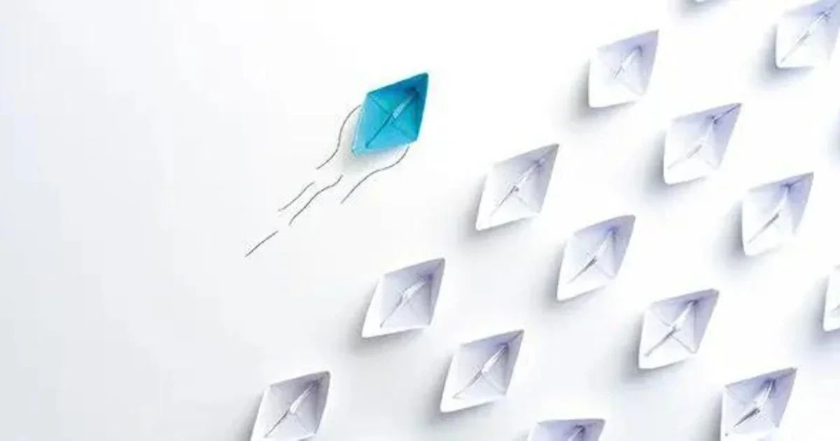 A single blue paper boat sailing ahead of a group of white paper boats.